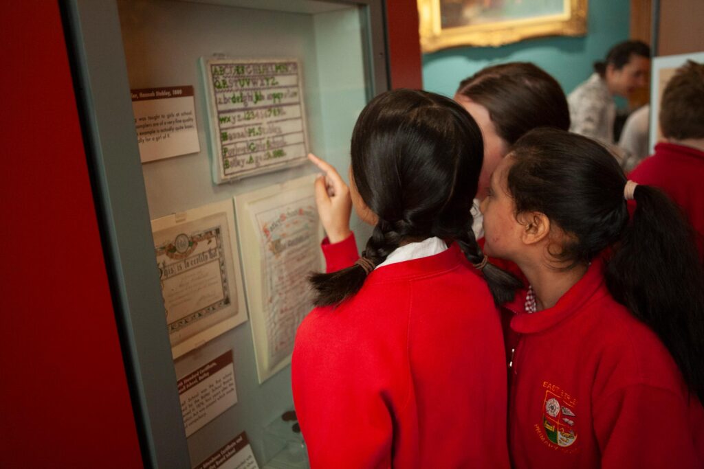 Three school girls look into a cabinet at a museum