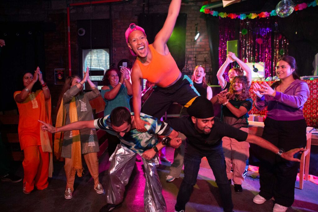 Group of diverse young people cheering and applauding an inside performance with bunting in the background