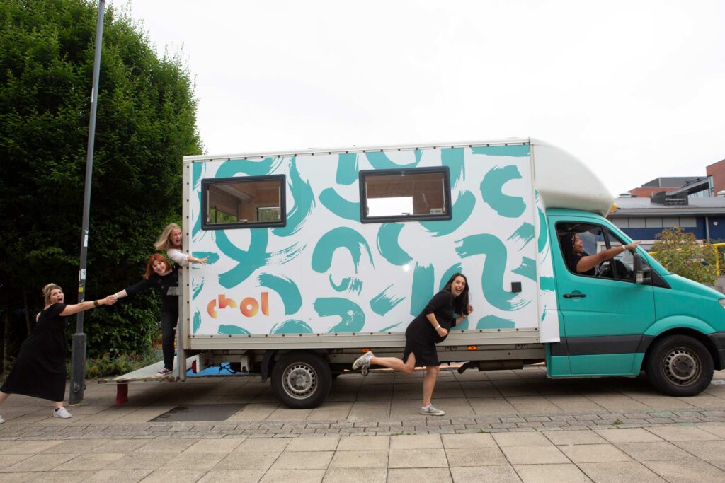 Three young women laughing next to a turquoise and white transit van