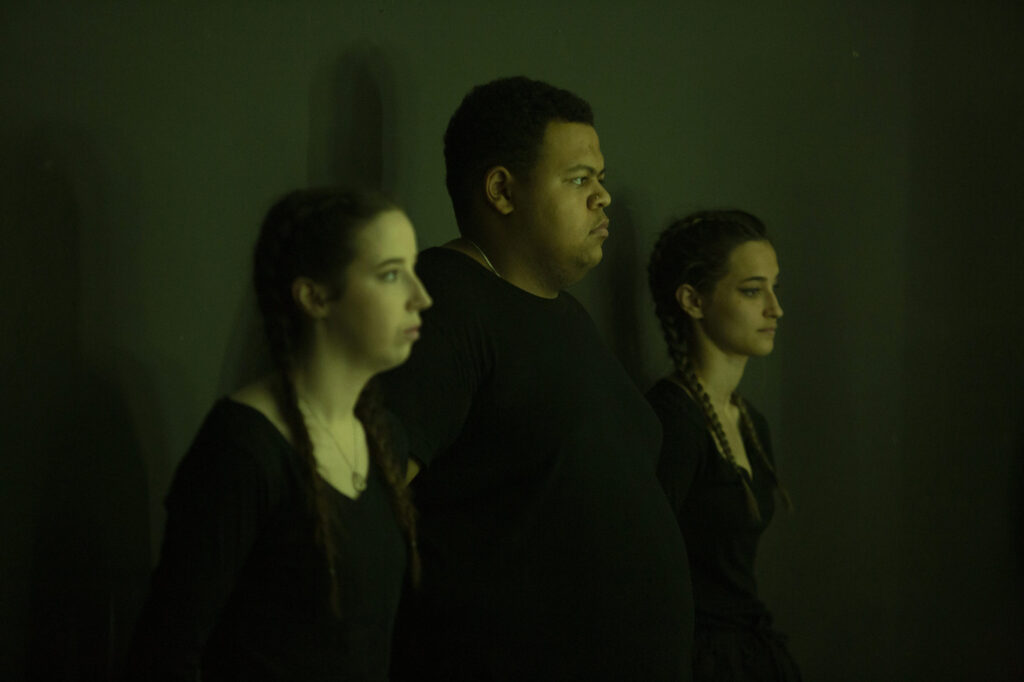 Three young diverse people standing on stage with a dark background